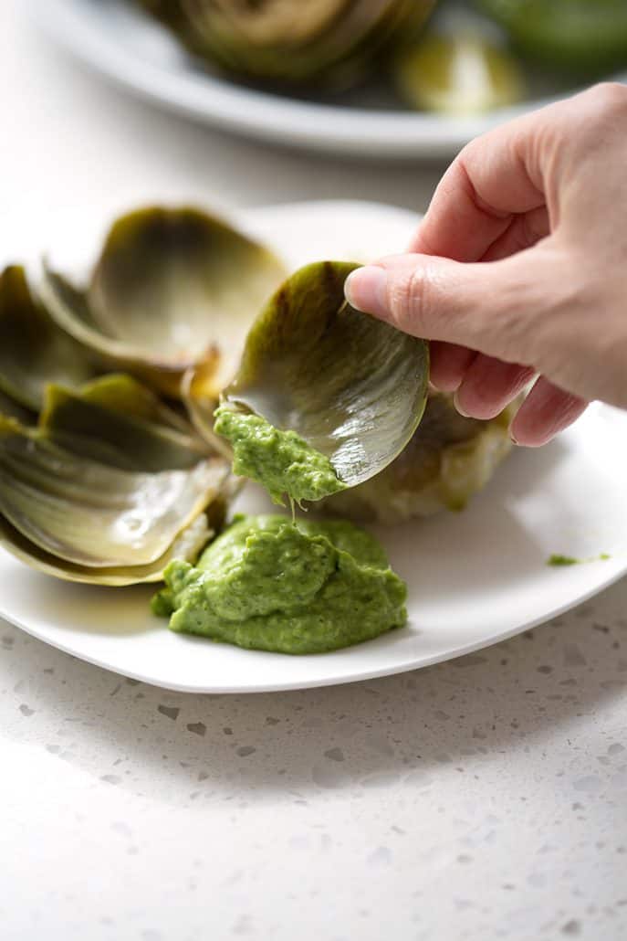 dipping artichoke leaf in green dip