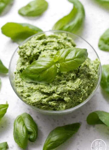 bowl of pesto surrounded by basil leaves
