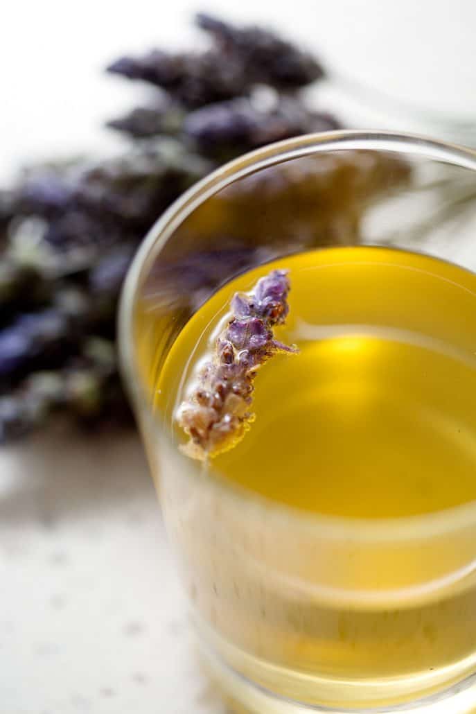 glass of kombucha tea with lavender flower floating in glass and bunches of lavender in the background
