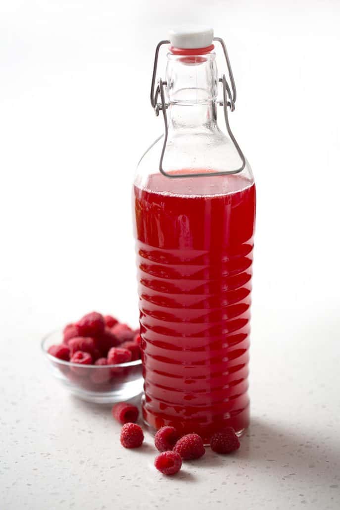 big bottle of raspberry thyme kombucha with raspberries on white background