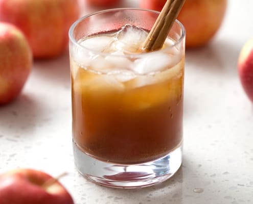 glass of kombucha in glass with apples and cinnamon stick on white background