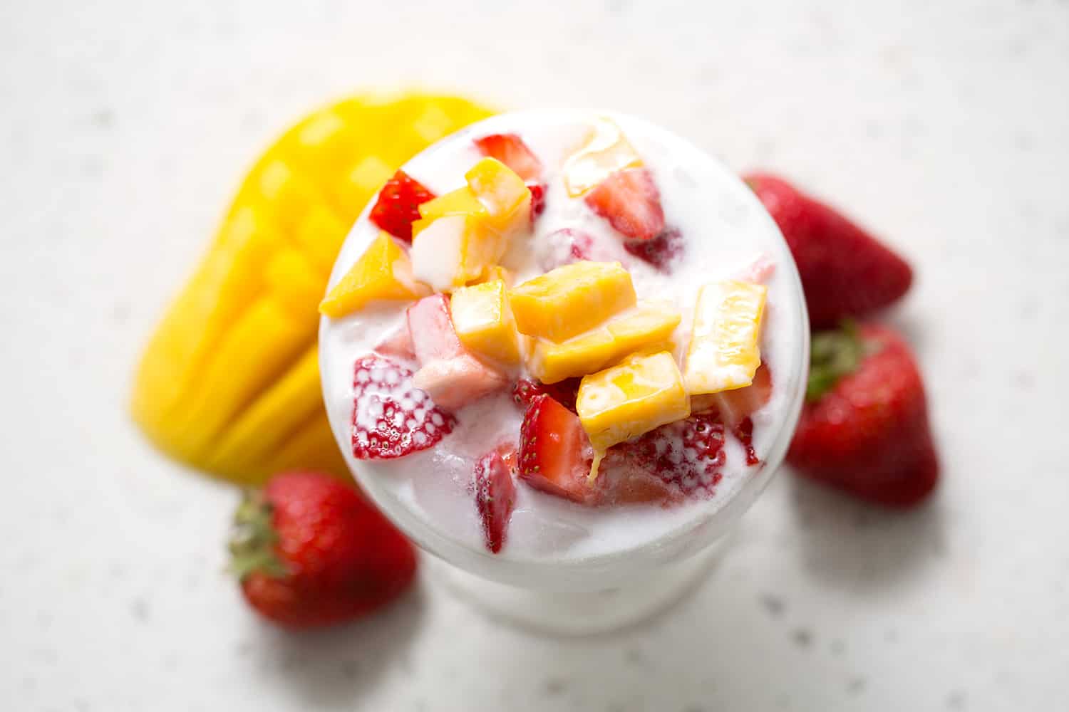 AIP Paleo shaved ice with mango, coconut milk, strawberries on white background.