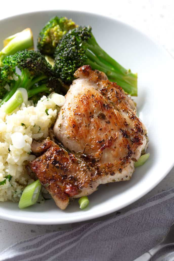 Chicken thigh resting on rice and broccoli on white bowl