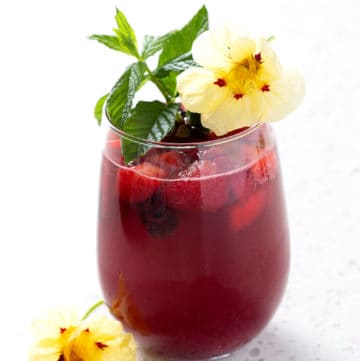 cocktail garnished with mint and flowers sitting on white background