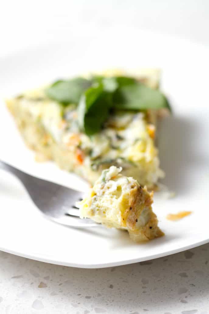slice of frittata with bite on fork and garnished with basil