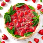 strawberry pie decorated with mint on white counter surrounded by strawberries