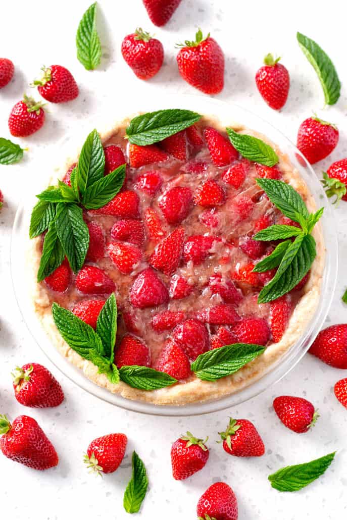 strawberry pie garnished with mint leaves and strawberries on white counter