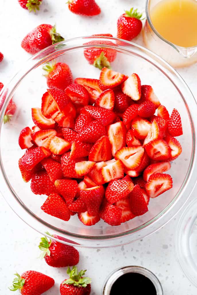 bowl of strawberries on white counter surrounded by strawberries and other ingredients