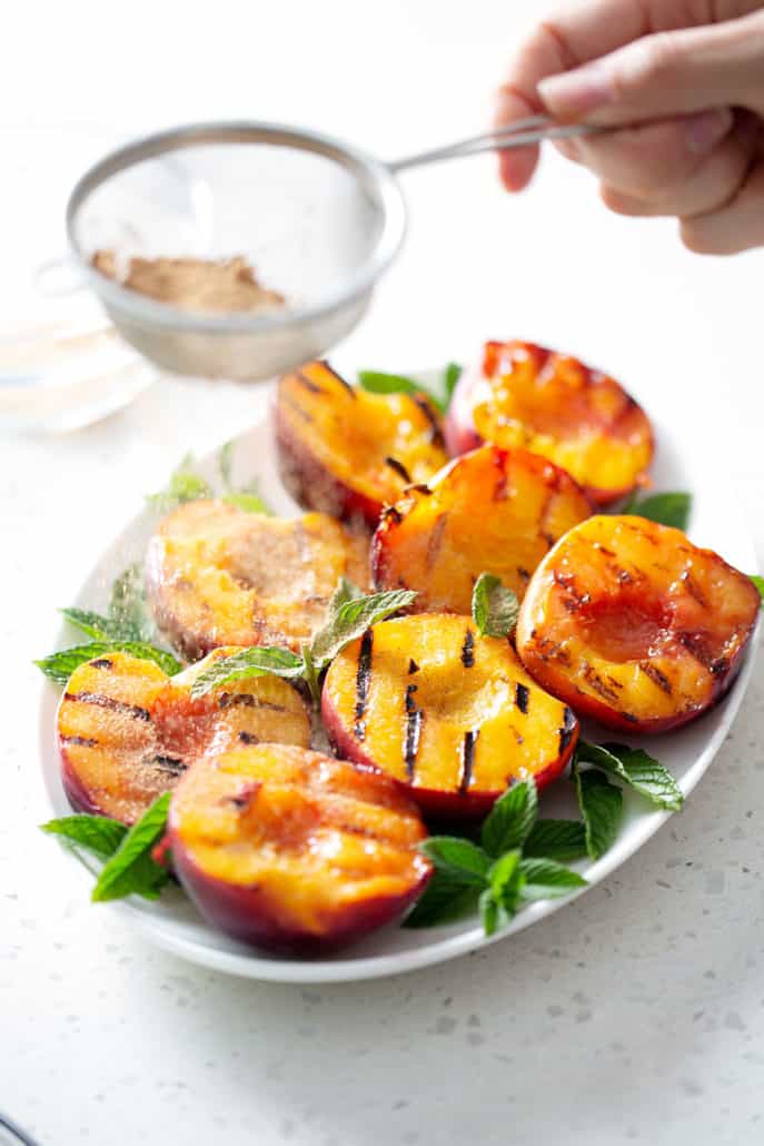 action shot of cinnamon sugar mixture being sprinkled on grilled peaches