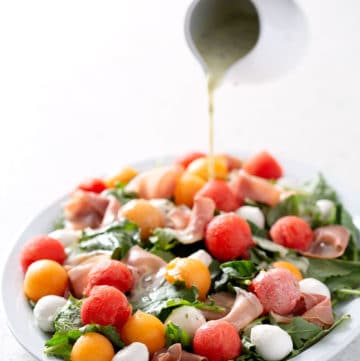 pouring dressing over platter of salad on white counter