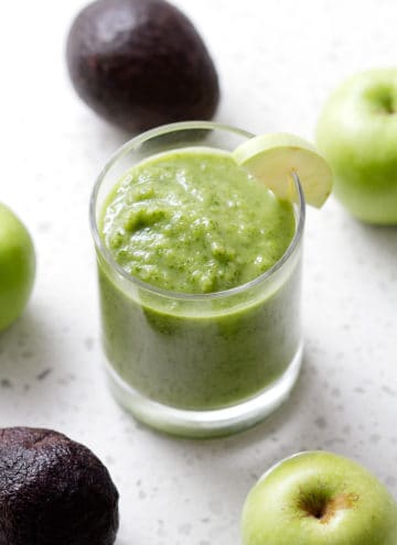 green smoothie in glass surrounded by avocados and green apples