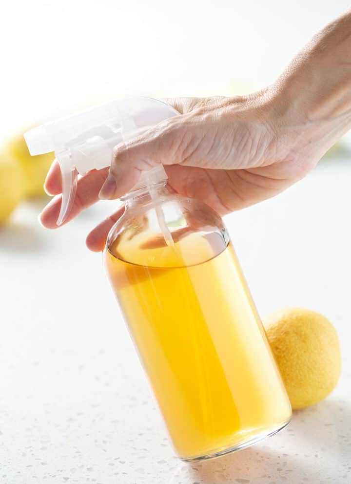holding spray bottle of yellow liquid on white background
