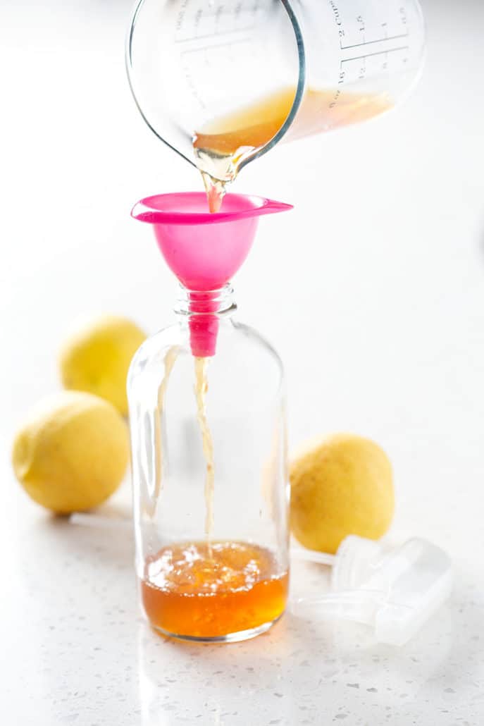 pouring yellow liquid into spray bottle surrounded by lemons on white background