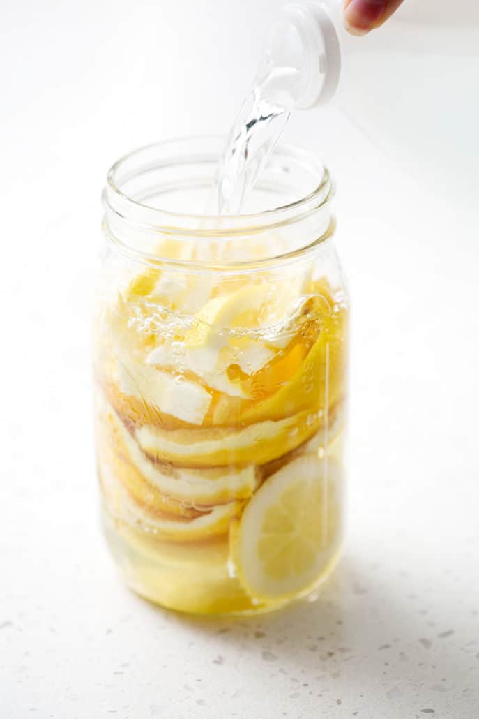 mason jar full of lemon rinds being filled with vinegar