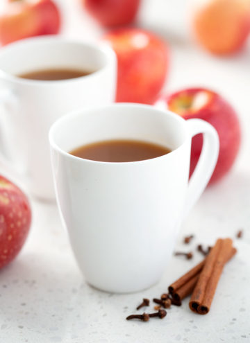 mug of apple cider surrounded by apples and spices