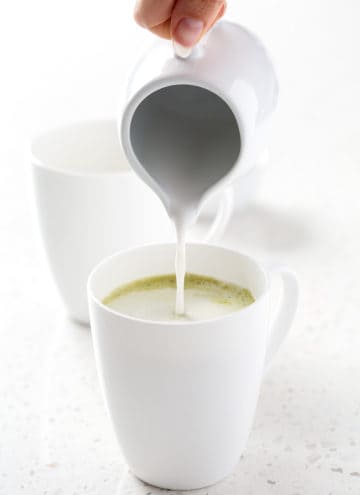 pouring coconut milk into mug of matcha green tea