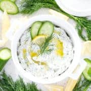 bowl of dairy free tzatziki surrounded by cucumbers, lemon and dill