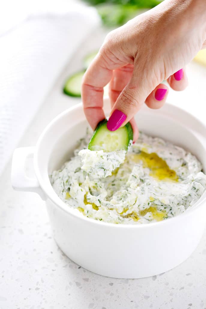 hand dipping cucumber into dairy free tzatziki