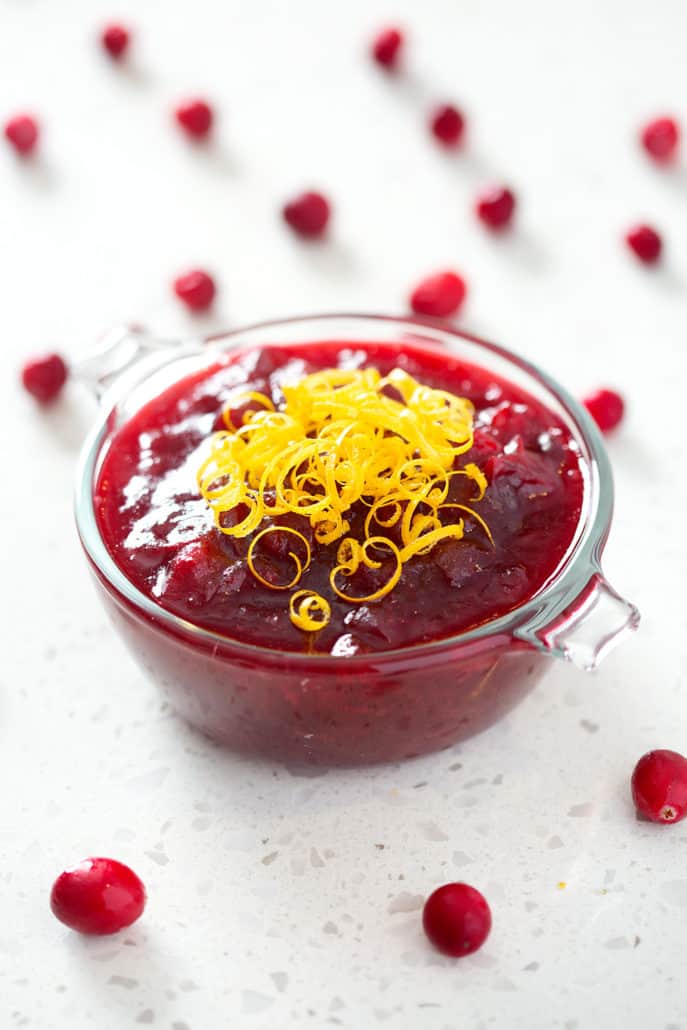 bowl of cranberry sauce garnished with orange zest surrounded by